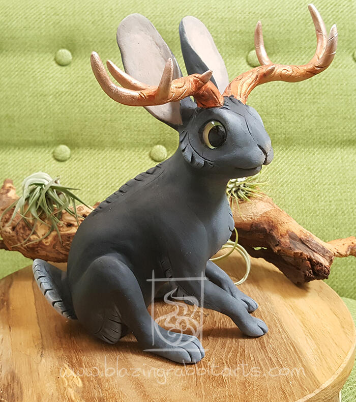 Black Jackalope Sculpture of a black Jackalope with copper horns sitting.